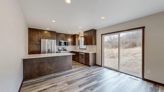 kitchen with light wood finished floors, light countertops, decorative backsplash, appliances with stainless steel finishes, and a sink