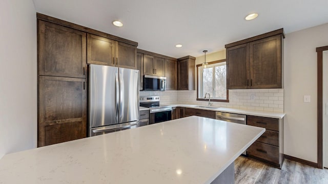 kitchen with appliances with stainless steel finishes, backsplash, a sink, and dark brown cabinetry