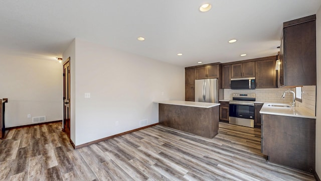 kitchen with tasteful backsplash, light countertops, appliances with stainless steel finishes, a sink, and dark brown cabinetry