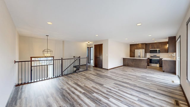 kitchen featuring light wood-style flooring, stainless steel appliances, open floor plan, light countertops, and an inviting chandelier