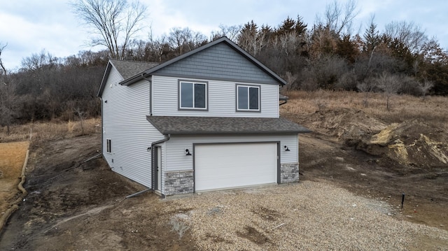 view of side of home featuring driveway, stone siding, and roof with shingles