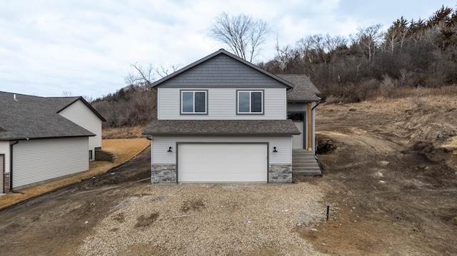 exterior space with dirt driveway, stone siding, a shingled roof, and an attached garage