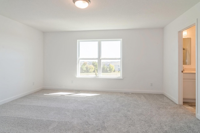 spare room featuring carpet, a sink, and baseboards