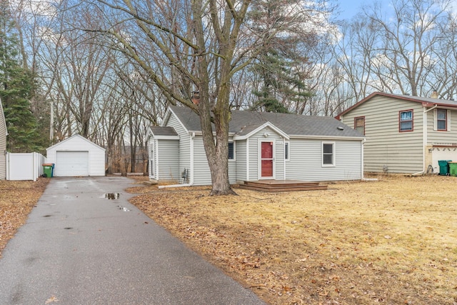 view of front facade featuring a detached garage, fence, roof with shingles, an outbuilding, and driveway