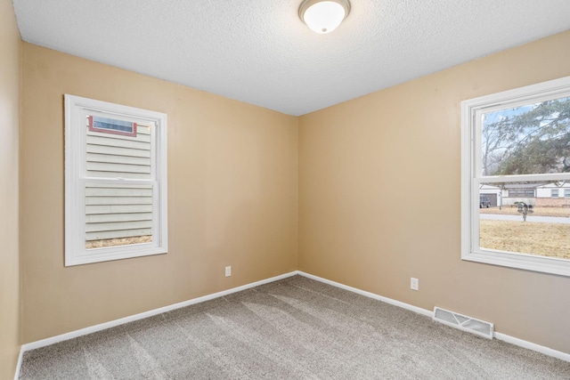 carpeted spare room with baseboards, visible vents, and a textured ceiling