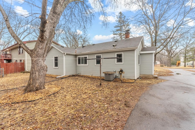 rear view of property with central AC unit, a chimney, and fence