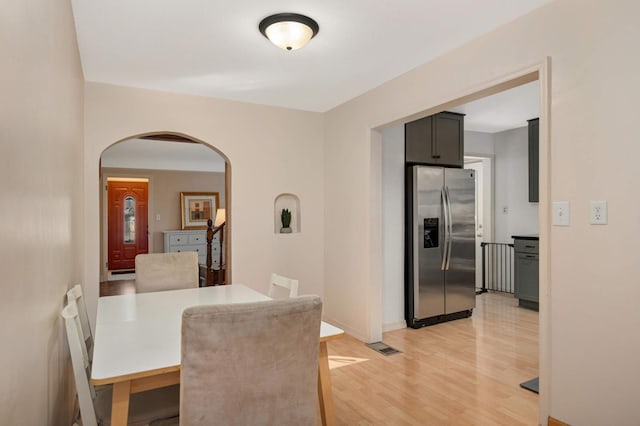 dining space featuring light wood finished floors, baseboards, stairs, and arched walkways