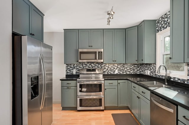 kitchen with light wood finished floors, decorative backsplash, stainless steel appliances, green cabinets, and a sink