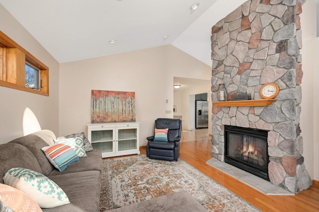 living area featuring vaulted ceiling, a stone fireplace, and wood finished floors