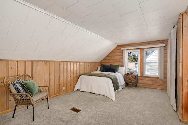 bedroom featuring lofted ceiling, wood walls, visible vents, and light colored carpet