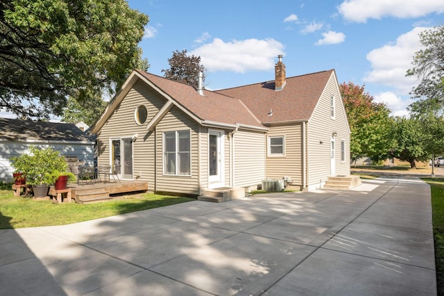 back of house with roof with shingles, a chimney, central AC unit, a deck, and driveway