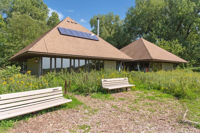 rear view of house with a shingled roof and solar panels