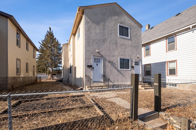 rear view of house with entry steps, a fenced backyard, and stucco siding