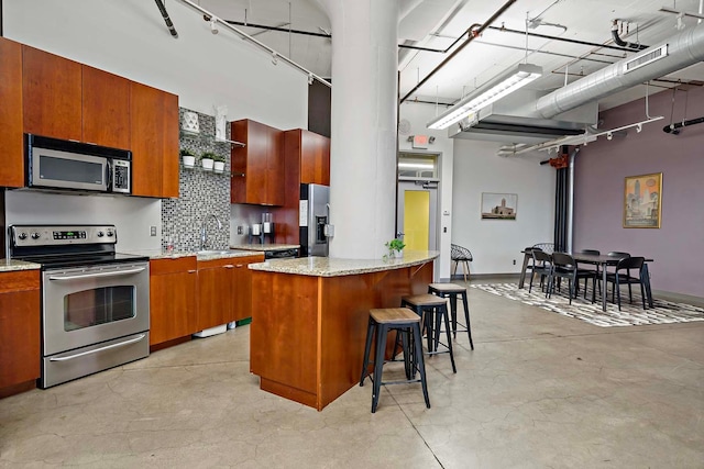 kitchen with a kitchen breakfast bar, brown cabinets, a towering ceiling, and stainless steel appliances