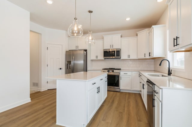 kitchen with light wood-type flooring, a sink, a kitchen island, appliances with stainless steel finishes, and decorative backsplash