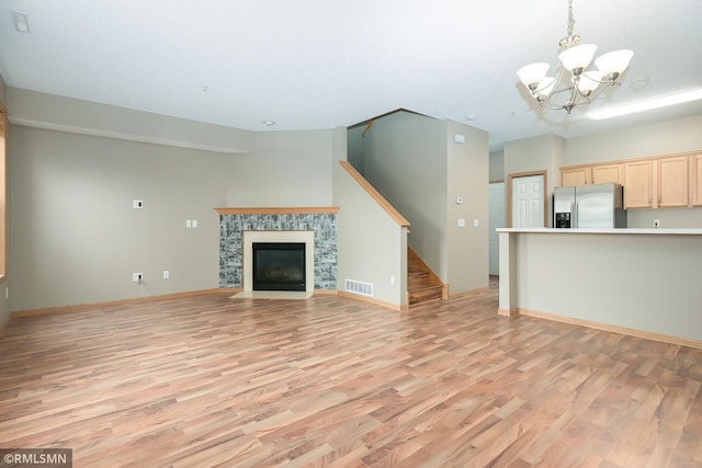 unfurnished living room featuring a fireplace with flush hearth, light wood-type flooring, visible vents, and stairway