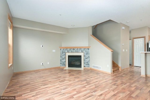 unfurnished living room with visible vents, baseboards, a fireplace with flush hearth, stairs, and light wood-style floors