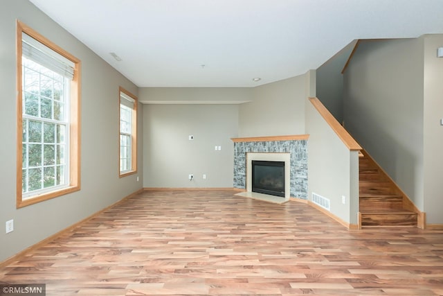 unfurnished living room featuring a healthy amount of sunlight, a fireplace with flush hearth, visible vents, and wood finished floors