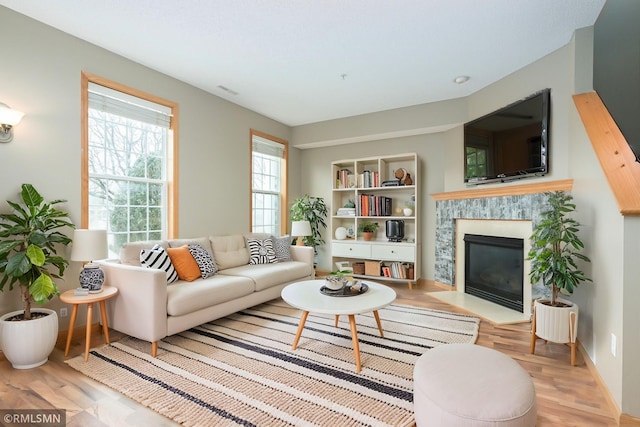 living area with a fireplace with flush hearth, light wood-style flooring, and baseboards