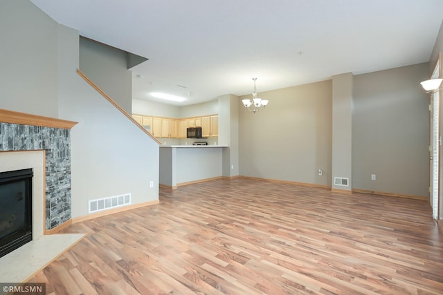 unfurnished living room featuring a fireplace with flush hearth, visible vents, light wood-style flooring, and a notable chandelier