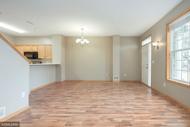 unfurnished living room featuring baseboards, light wood-style flooring, visible vents, and an inviting chandelier