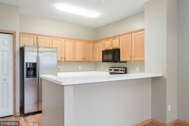 kitchen with stainless steel fridge, range, a peninsula, light brown cabinetry, and black microwave