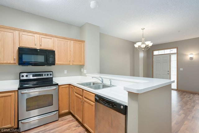 kitchen with a peninsula, a sink, light wood-style floors, light countertops, and appliances with stainless steel finishes