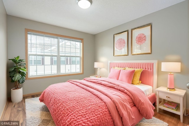 bedroom featuring a textured ceiling, baseboards, and wood finished floors