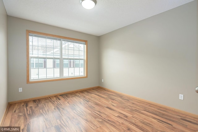 empty room with light wood-style flooring, baseboards, and a textured ceiling