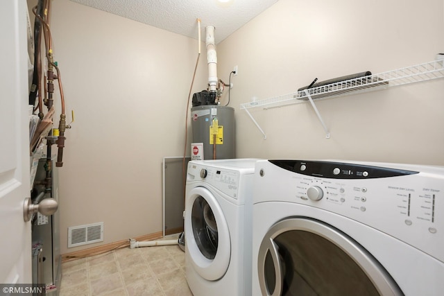 washroom featuring water heater, visible vents, a textured ceiling, washer and dryer, and laundry area