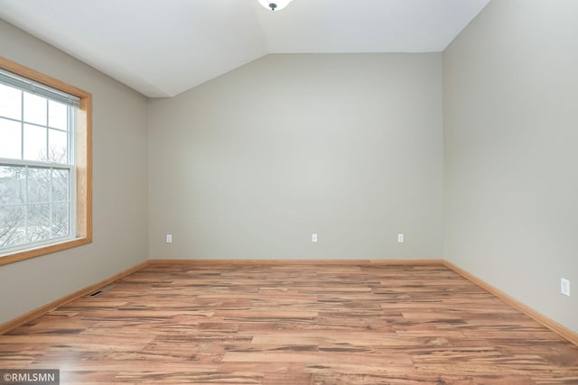 empty room with lofted ceiling, light wood finished floors, baseboards, and visible vents