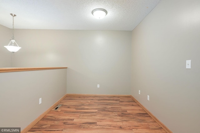 spare room featuring light wood finished floors, baseboards, and a textured ceiling