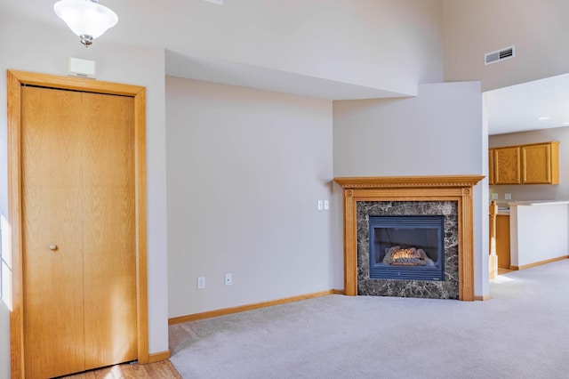 unfurnished living room with light carpet, baseboards, a premium fireplace, and visible vents