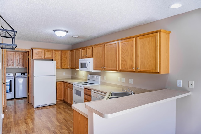 kitchen with white appliances, a peninsula, light countertops, washer and dryer, and a sink