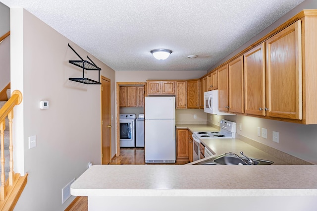 kitchen featuring a textured ceiling, washing machine and dryer, a peninsula, white appliances, and light countertops