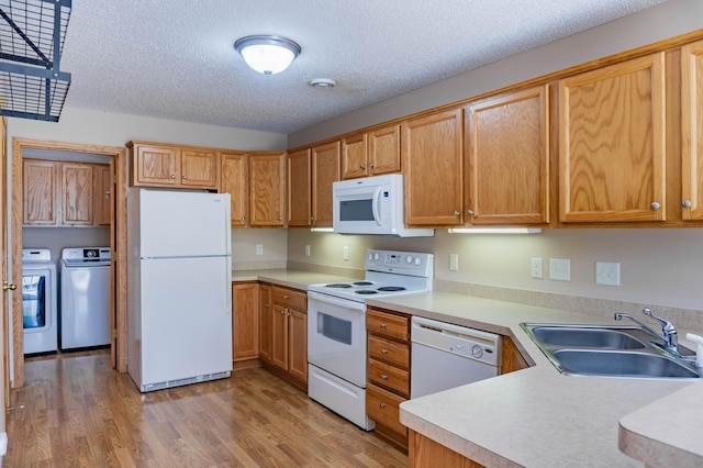 kitchen featuring light wood finished floors, light countertops, washing machine and dryer, a sink, and white appliances