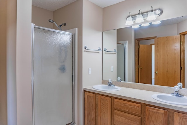 full bath with a textured ceiling, double vanity, a stall shower, and a sink