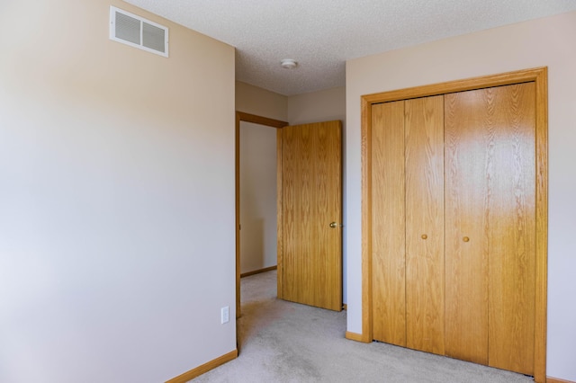 unfurnished bedroom with a textured ceiling, carpet flooring, visible vents, baseboards, and a closet