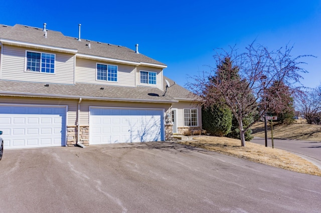 view of front of house featuring stone siding, a shingled roof, an attached garage, and aphalt driveway