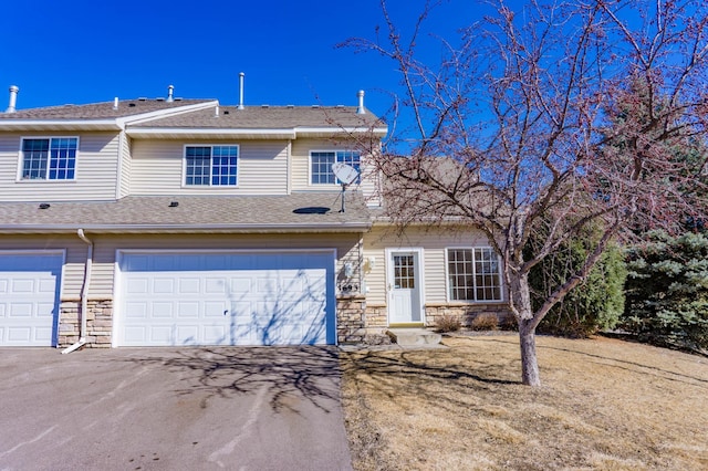 townhome / multi-family property featuring an attached garage, stone siding, a shingled roof, and aphalt driveway