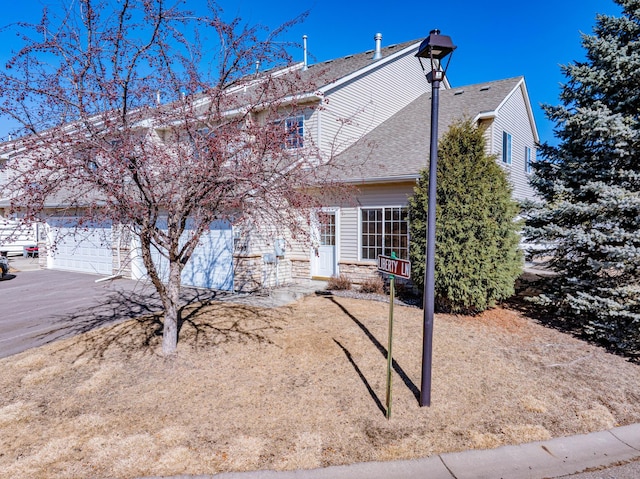 view of front of property featuring driveway, stone siding, a shingled roof, and a garage