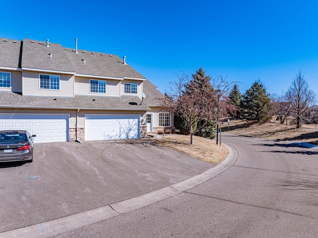 exterior space with a garage, stone siding, a shingled roof, and driveway