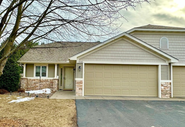 craftsman house with an attached garage, stone siding, a shingled roof, and aphalt driveway