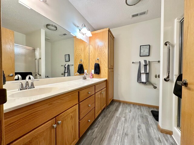bathroom with a textured ceiling, wood finished floors, a sink, visible vents, and a stall shower