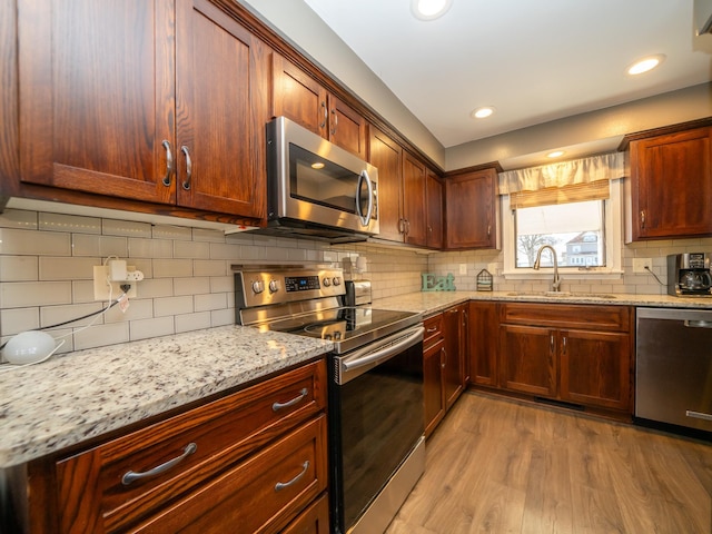 kitchen with a sink, light stone counters, light wood-style floors, and appliances with stainless steel finishes