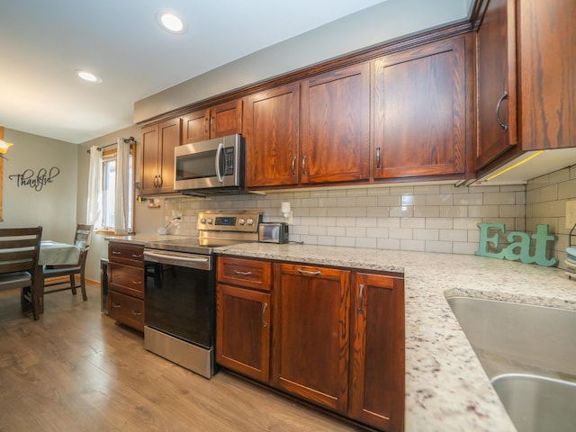 kitchen with light stone countertops, light wood finished floors, a sink, decorative backsplash, and appliances with stainless steel finishes