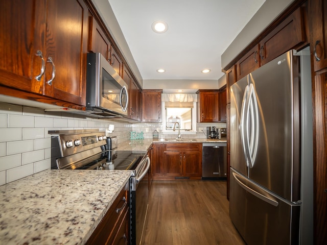 kitchen with light stone countertops, dark wood finished floors, decorative backsplash, appliances with stainless steel finishes, and a sink