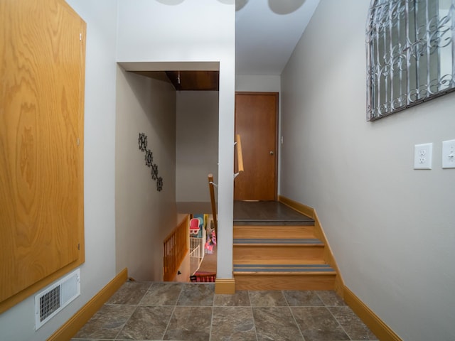 stairway with visible vents, stone finish flooring, and baseboards