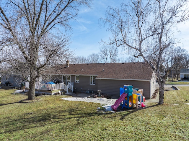 rear view of house with a deck, a playground, a yard, and a shingled roof