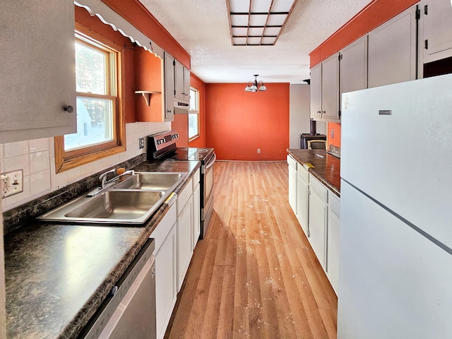 kitchen featuring dark countertops, light wood-style flooring, decorative backsplash, appliances with stainless steel finishes, and a sink